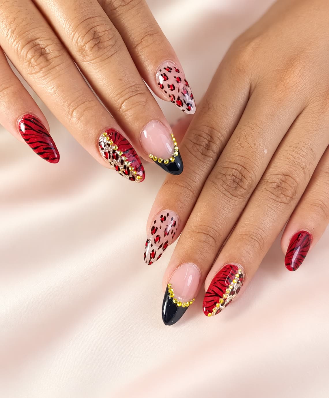 Uñas almendra con diseño animal print rojo, cristales dorados y detalles negros